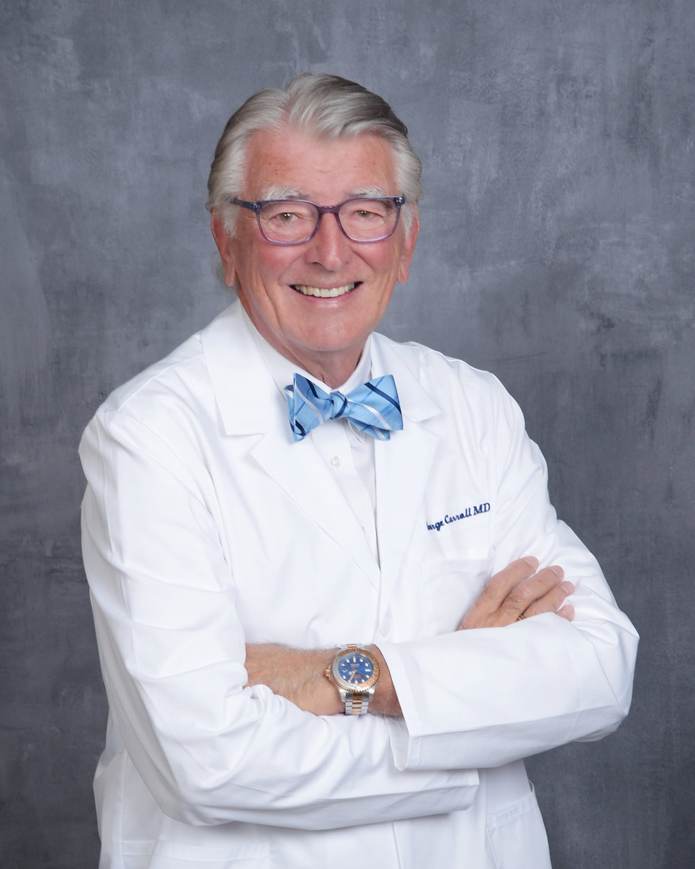 Dr. George W. Carroll, MD, smiling, in a white coat with his arms folded