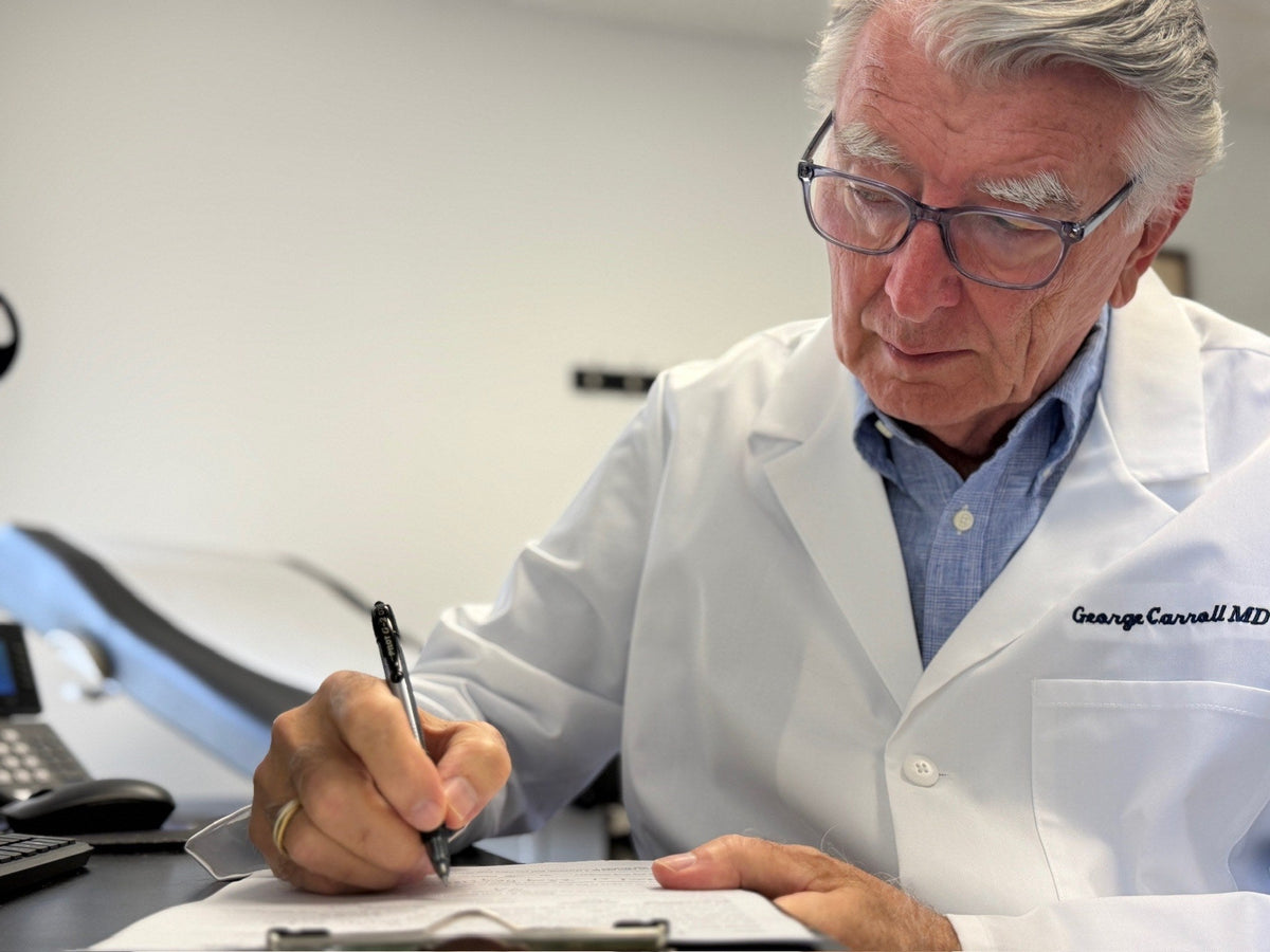 Dr. George W. Carroll, MD, writing on a clipboard at his desk in his Maitland exam room.