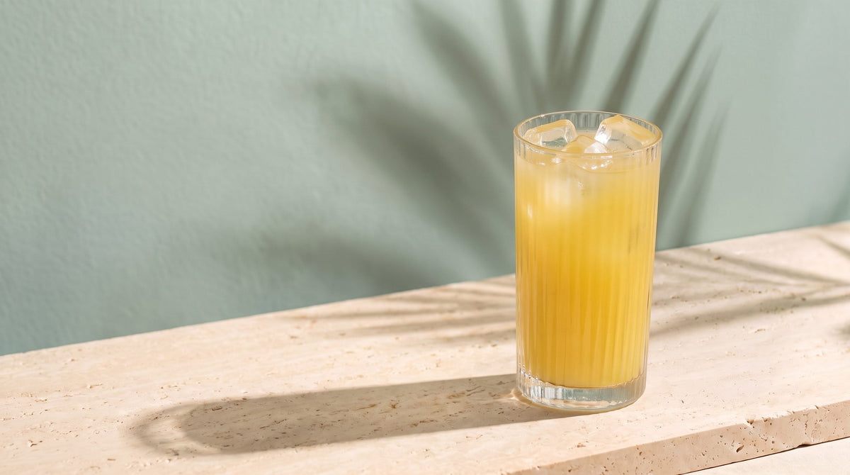 A ribbed glass of iced golden drink on a travertine ledge in morning sun