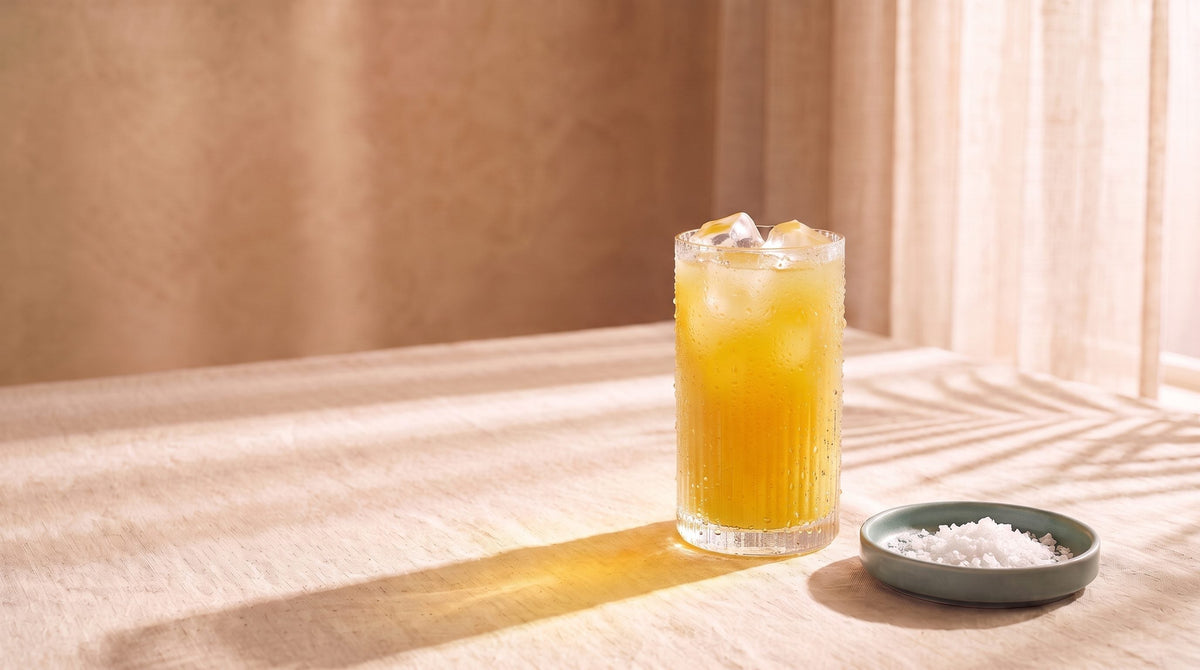 A ribbed glass of golden drink with ice beside a small teal dish of sea-salt flakes