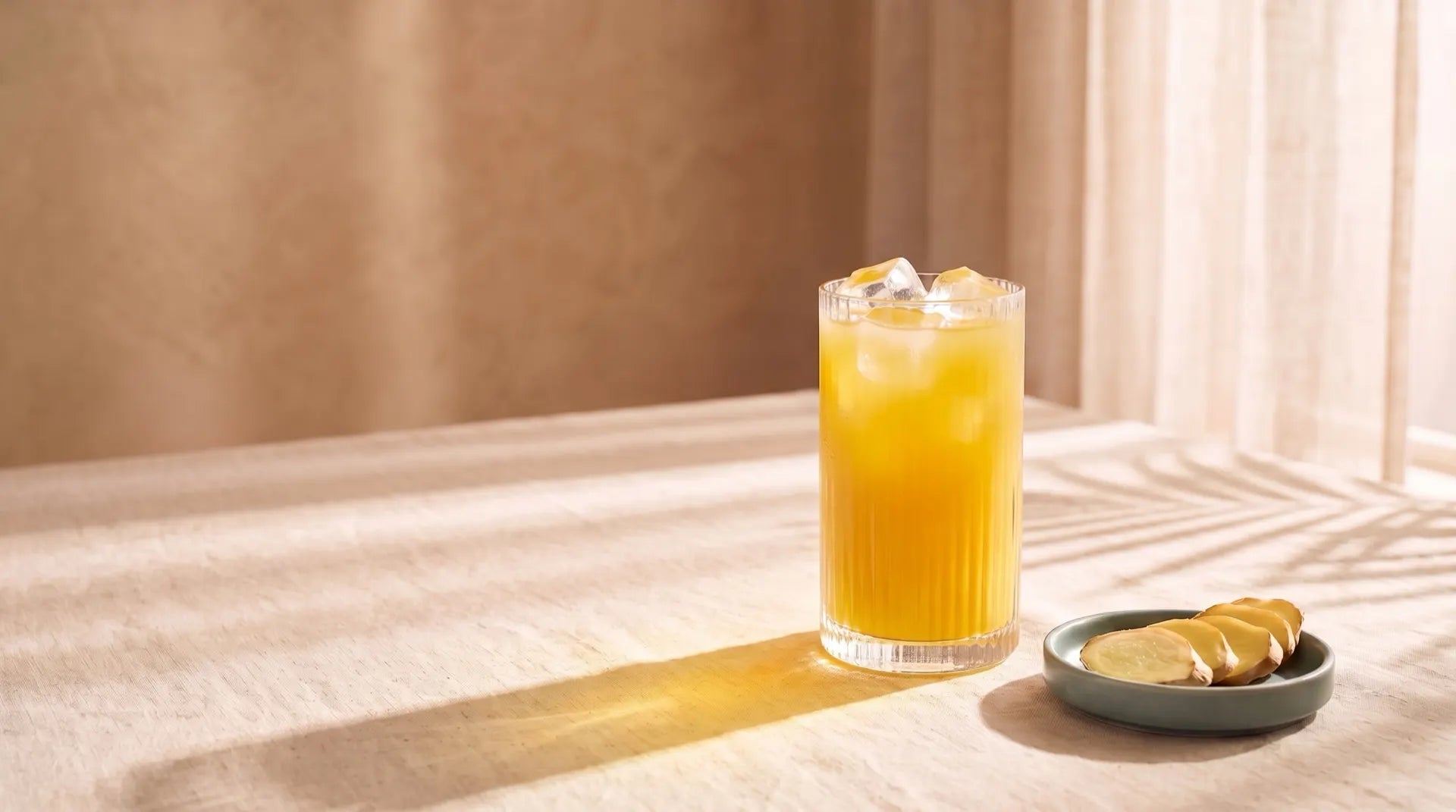 A tall ribbed glass of cloudy golden GLPrelief drink with ice on a linen table in morning sun, beside a small dish of fresh ginger