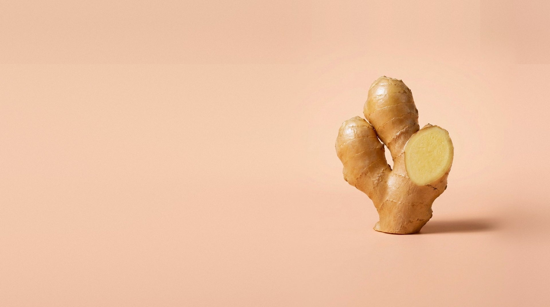 A fresh ginger root with one cut face, on an apricot backdrop