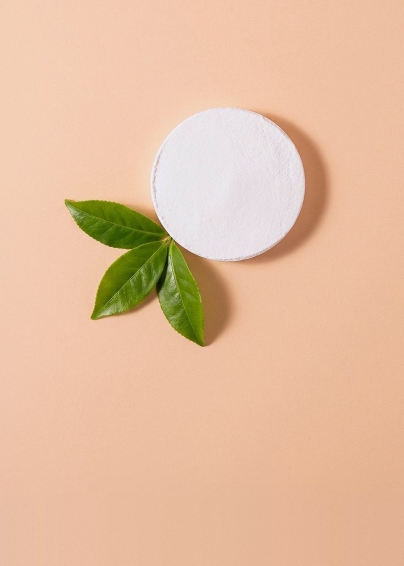 White L-theanine powder pressed into a disc beside three fresh tea leaves