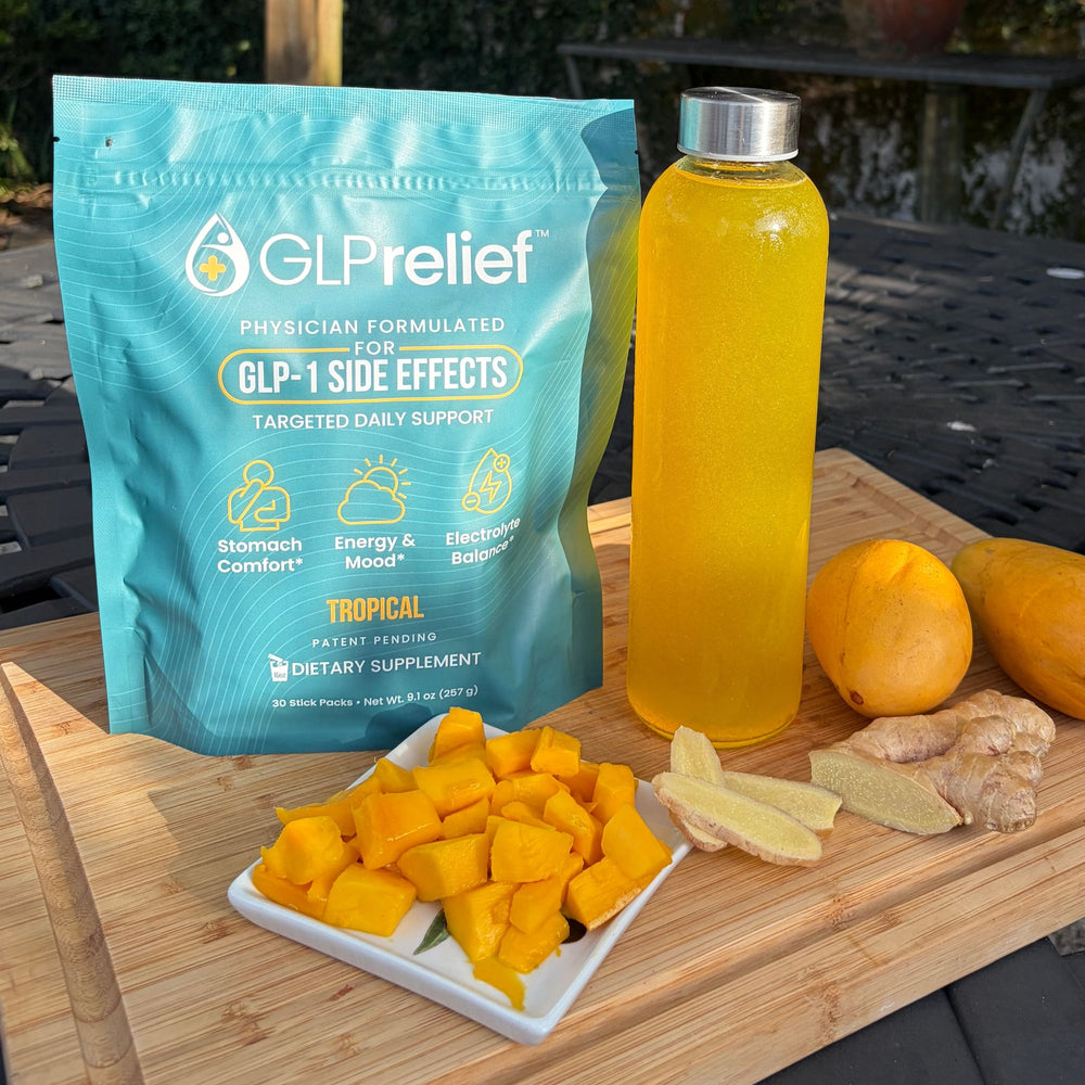 A GLPrelief tropical drink mix bag beside a glass bottle of the mixed drink, with fresh mango and sliced ginger on a cutting board outdoors
